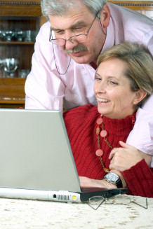 Äldre par gosar framför datorn